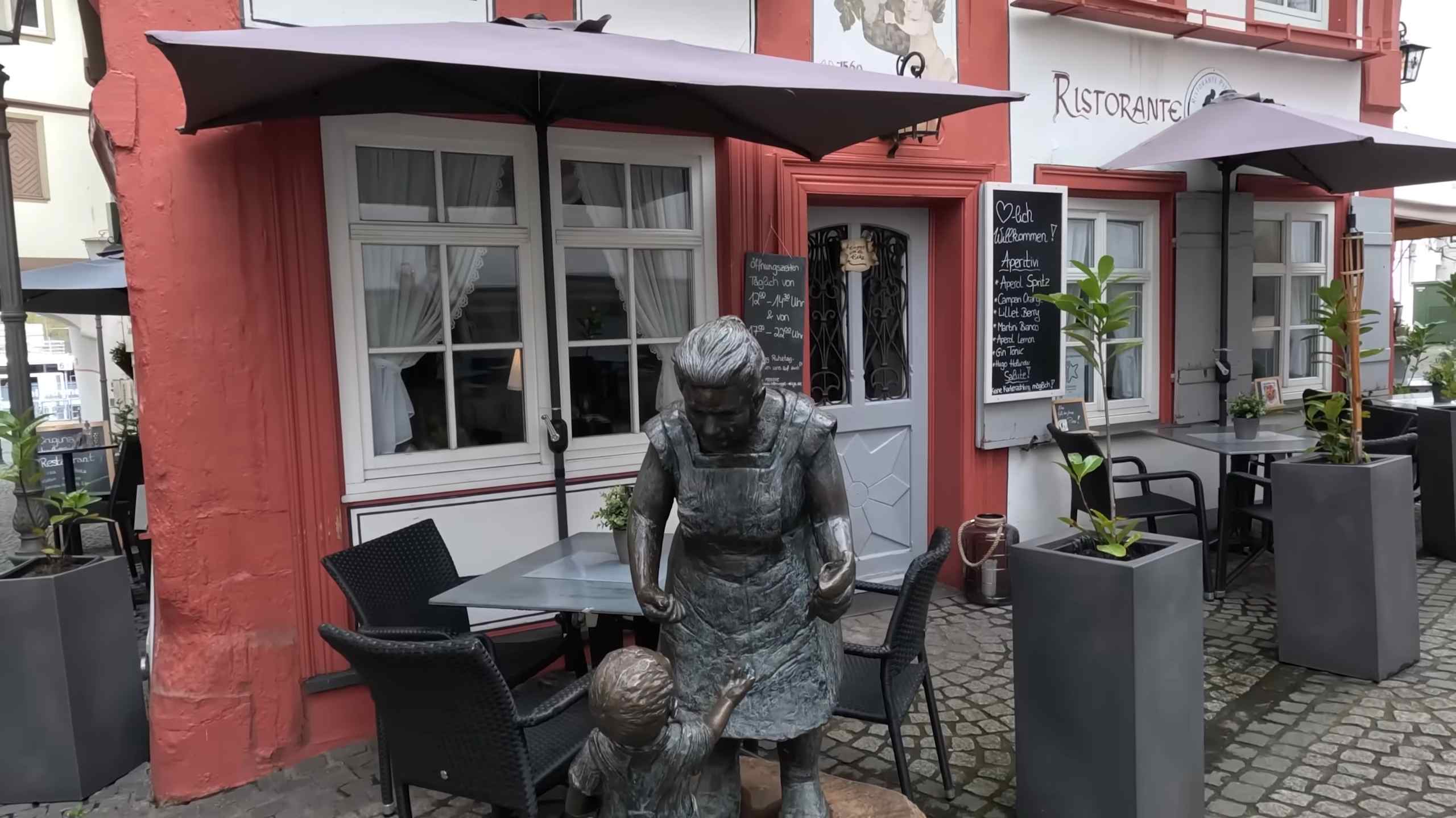 Skulptura dece ispred restorana u starom delu Koblenca, okružena tradicionalnim zgradama